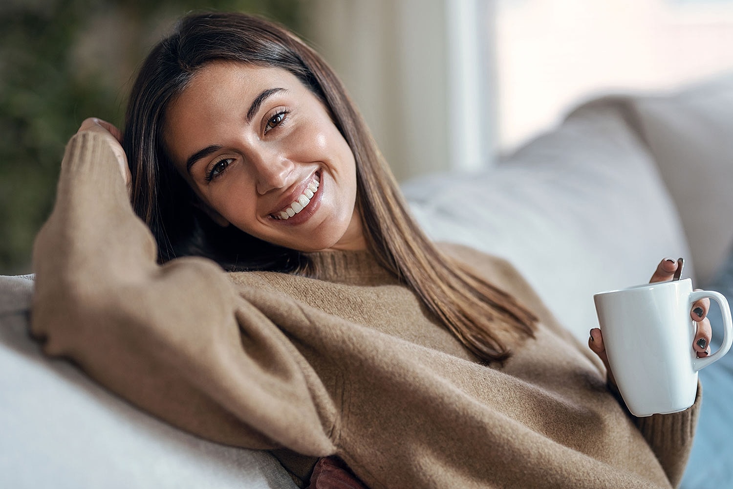 Smiling woman holding a mug on couch.